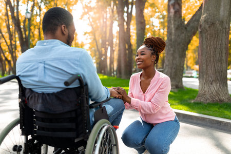 Affectionate black woman holding her paraplegic husbands hand, expressing love at autumn parkの写真素材