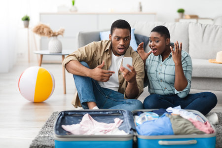 Black Couple Using Phone Reading Message About Flight Cancellation Indoorの写真素材