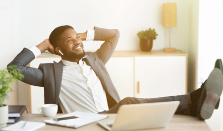 Relaxed african businessman enjoy listening music in earphones at workplaceの写真素材