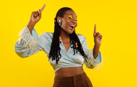 Black Woman Listening To Music Via Earbuds Over Yellow Background