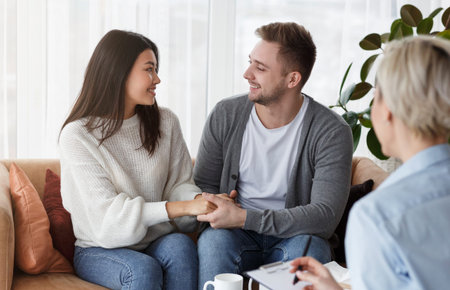 Happy Couple Holding Hands Reconciling After Therapy Sitting In Officeの写真素材
