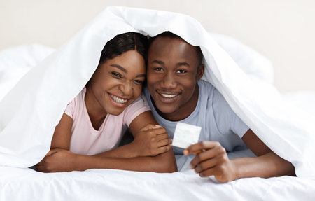 Happy black couple hiding under blanketの写真素材
