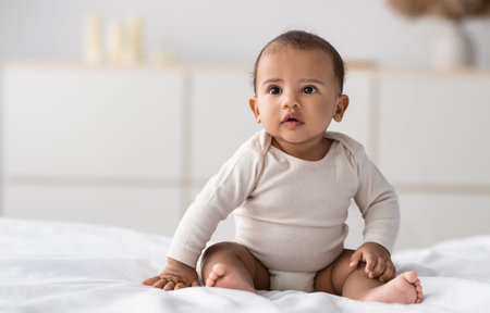 Cute little African American infant sitting on bedの写真素材