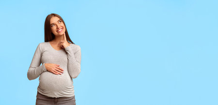 Happy Pregnant Woman Thinking Standing Over Gray Studio Backgroundの写真素材