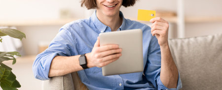 Young Man Makes Online Purchase Using Tablet and Credit Card in Modern Living Room