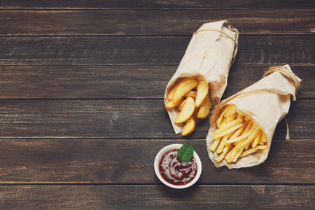 Fries and potato wedges wrapped takeaway at wood