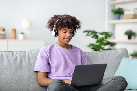 Remote education. Black teen guy in headphones having online lesson, participating in webinar on...