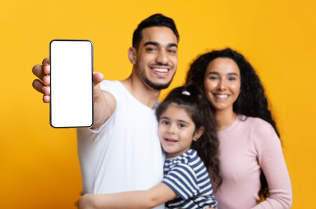 Happy middle eastern family of three showing blank smartphone screen for mockup