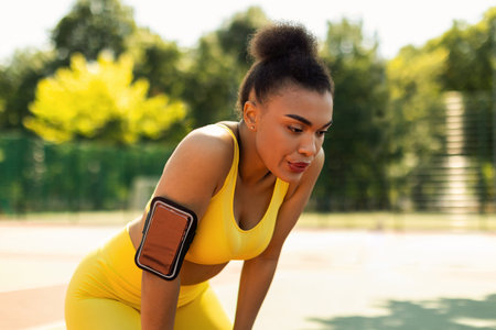 Sporty black woman in yellow sportswear resting after runの写真素材