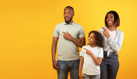 Young family of three posing and pointing aside at copy space on yellow background, studio shotの写真素材