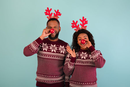 Xmas fun. Playful black couple holding Christmas baubles near their noses over blue backgroundの写真素材