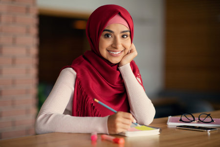 Cheerful young muslim lady in hijab planning day at cafeの写真素材