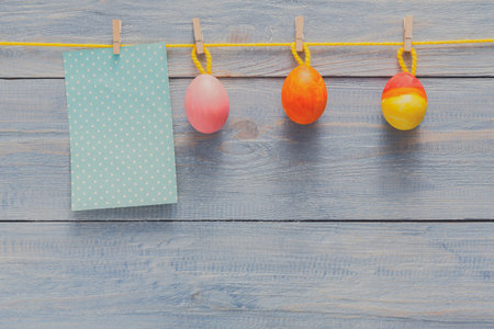 Colorful Easter Eggs Hanging on a String With a Blank Card on Wooden Backgroundの写真素材