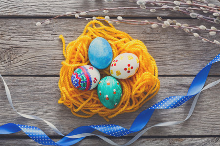 Colorful Easter Eggs Arranged on a Nest of Yellow Yarn With Ribbons and Spring Decor