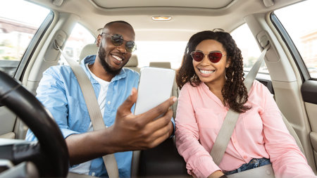 Happy black couple driving car and using smartphoneの写真素材