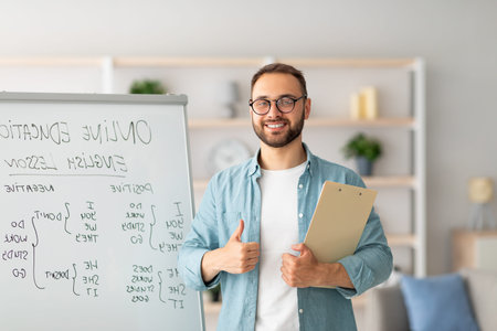 Positive male teacher showing thumb up gesture near blackboard, recommending new online English...