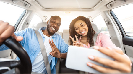 Happy black couple driving car and taking selfie on smartphoneの写真素材