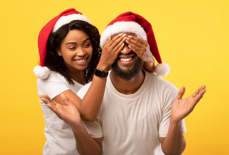 Happy african american lady standing behind man and closing his eyes, yellow studio backgroundの写真素材