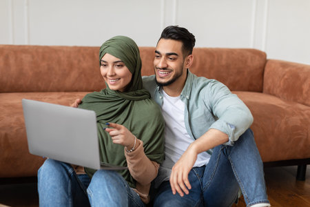 Happy muslim man and woman using laptop pointing at screenの写真素材