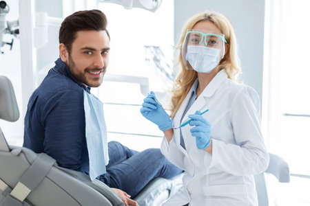 Patient and female doctor with dental tools looking at cameraの写真素材