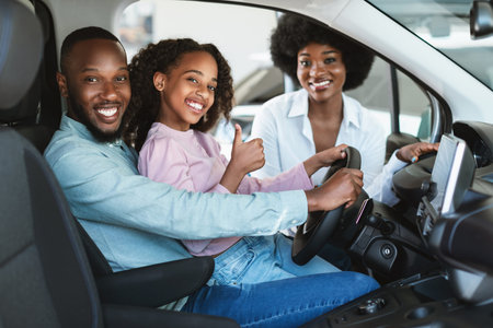 Cute black girl with her parents recommending auto dealership, sitting inside new car, showing thumb up gestureの写真素材