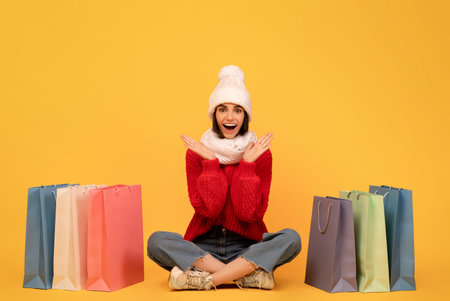 Shopaholic concept. Happy lady in knitted hat and sweater sitting among colorful shopping bags on...