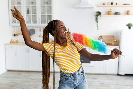 Emotional afro-american woman having fun while cleaning at kitchenの写真素材