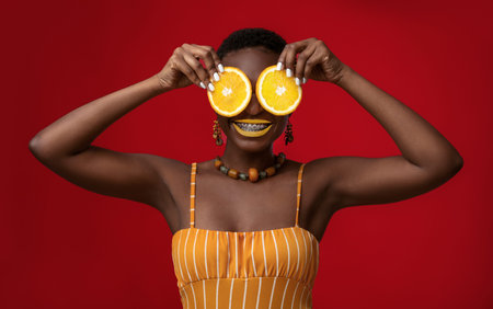 Joyful black lady holding orange circles over her eyesの写真素材