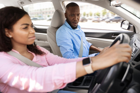 Scared instructor looking at serious focused black lady driver