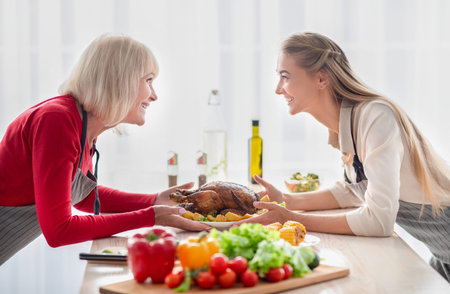 Happy young woman and her senior mother serving table with traditional festive turkey, having family holiday celebrationの写真素材