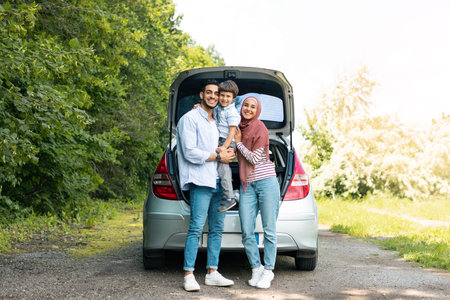 Rest outdoor from road, family journey at summer. Satisfied millennial arab man and lady in hijabの写真素材