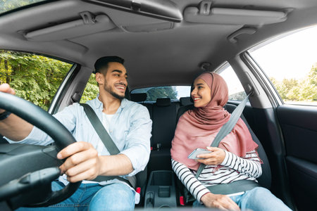Cheerful young middle eastern woman in hijab with smartphone and husband rides on car