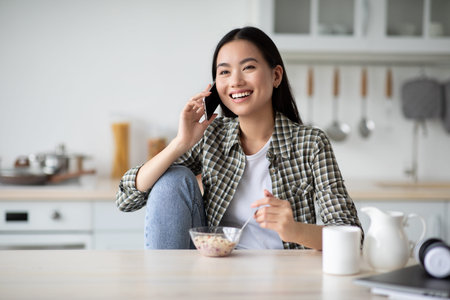 Young asian lady having breakfast and talking on phone