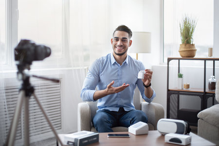 Arab male blogger promoting new model of wireless earphones, filming video review of modern gadget...