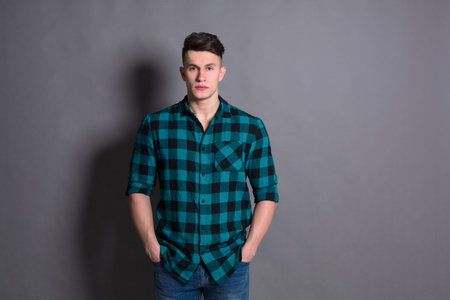 Young Man Posing Confidently in a Green Plaid Shirt Against a Grey Backgroundの写真素材