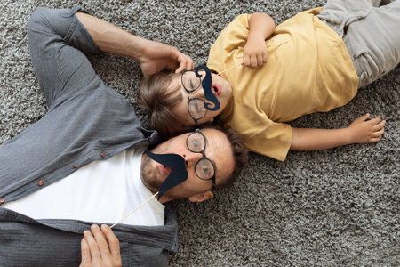 Movember concept. Funny surprised father and and little son wearing eyeglasses holding moustache photo props, top viewの写真素材