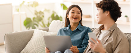 Couple Enjoying Time Together at Home While Using Laptop and Smartphoneの写真素材