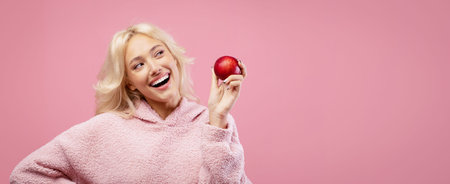 Woman Holds a Red Apple With a Smile in a Pink Background During a Bright Momentの写真素材