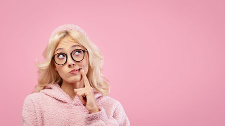 Young Woman Thinking With Finger on Chin in Front of Pink Background During Indoor Photo Sessionの写真素材