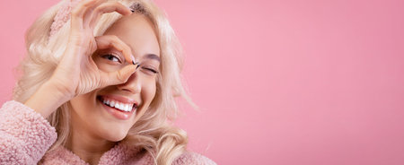 Smiling Woman Making a Playful Gesture in Front of a Pink Background During a Light Momentの写真素材