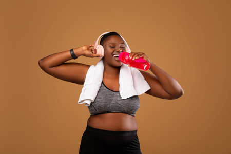 Young Black Woman Wearing Headphones Drinking Water At Studio