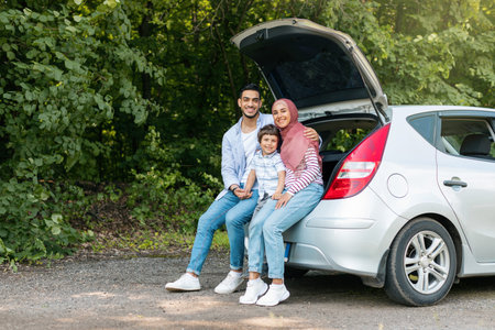 Rest and relax at road. Happy young arab male and female in hijab with small son sitting in car trunkの写真素材