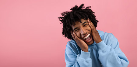 Cool black teenager holding his head in shock, screaming OMG, cannot believe his luck on pink studio backgroundの写真素材