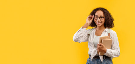 Student Holds Books and Smiles in Front of a Bright Yellow Background During Daytimeの写真素材