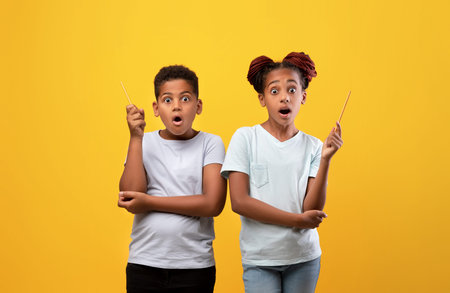 Amazed black girl and boy raising pencils upの写真素材