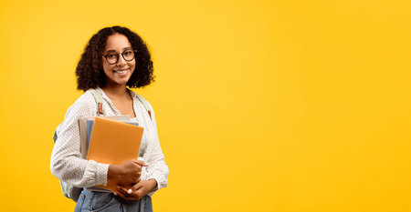 Student Stands Against Yellow Background Holding Notebooks and Smiling for a School-Related Moment