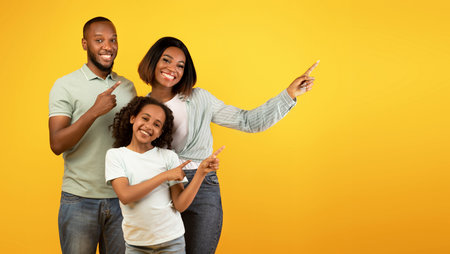 Positive african american family of three pointing aside at free space on yellow background, bannerの写真素材
