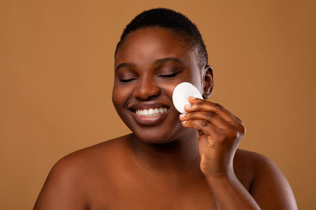 Portrait of happy black woman cleaning skin by cotton pad