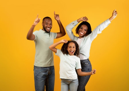 Overjoyed african american family of three dancing and enjoying favorite music together on yellow studio backgroundの写真素材