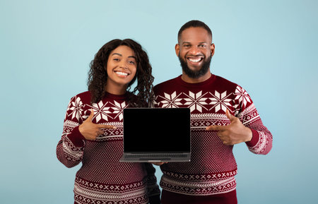 Christmas online shopping. Happy african american couple showing laptop with empty screen, pointing on itの写真素材